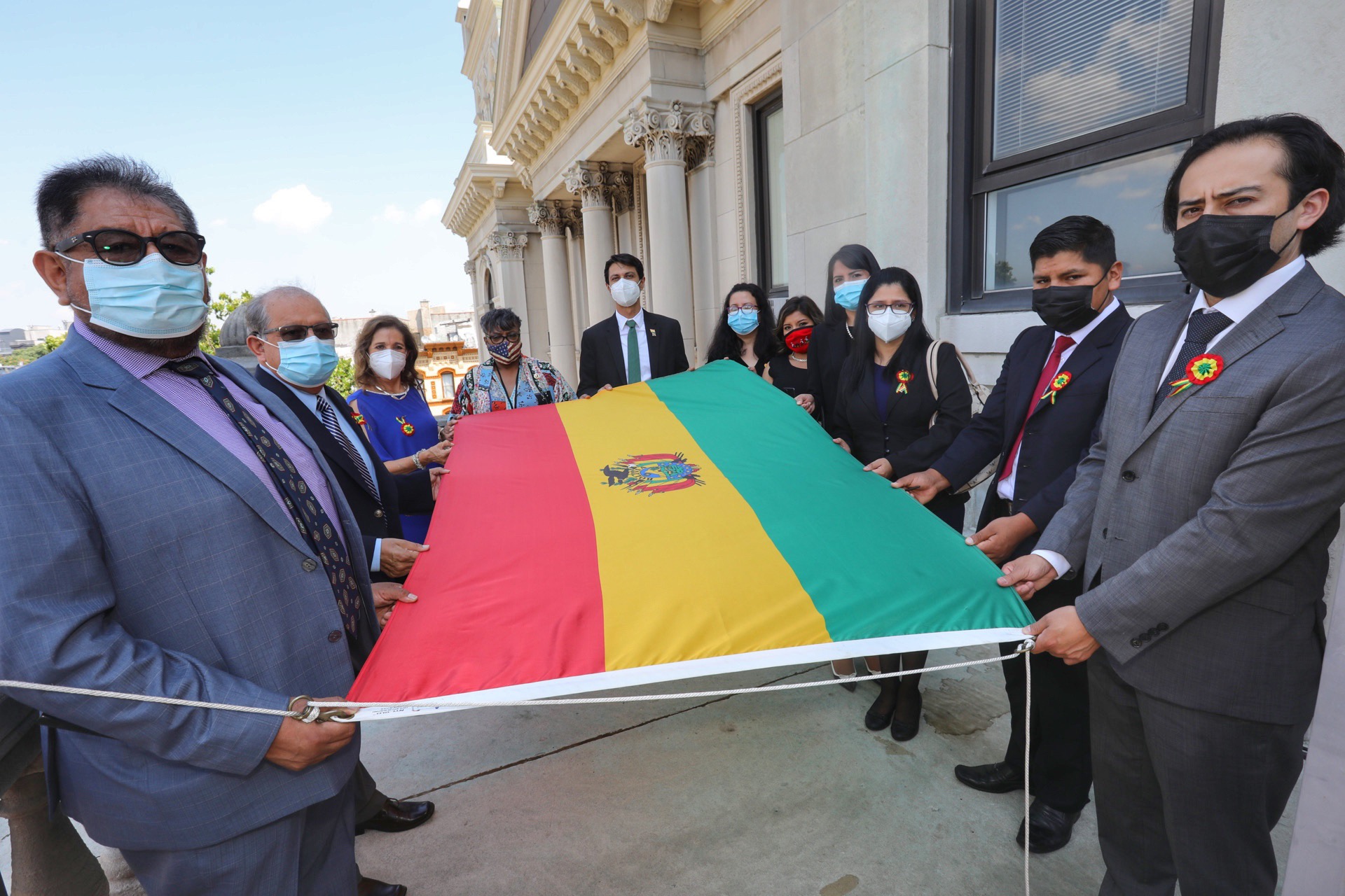 Bolivian Flag Raising Group of people hold the flag before it is raised. The national flag of Bolivia is described as a tricolor rectangle, with the colors red, yellow and green. The nationa seal appears in the center of the yellow stripe.