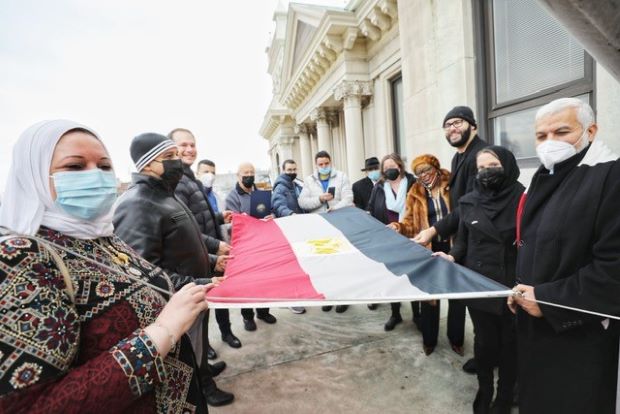 All attendees standing holding the Egyptian Flag on the City Hall Balcony.