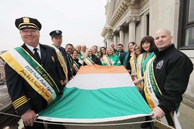 A group of people holding the flag of Ireland prior to it being raised at city hall. 